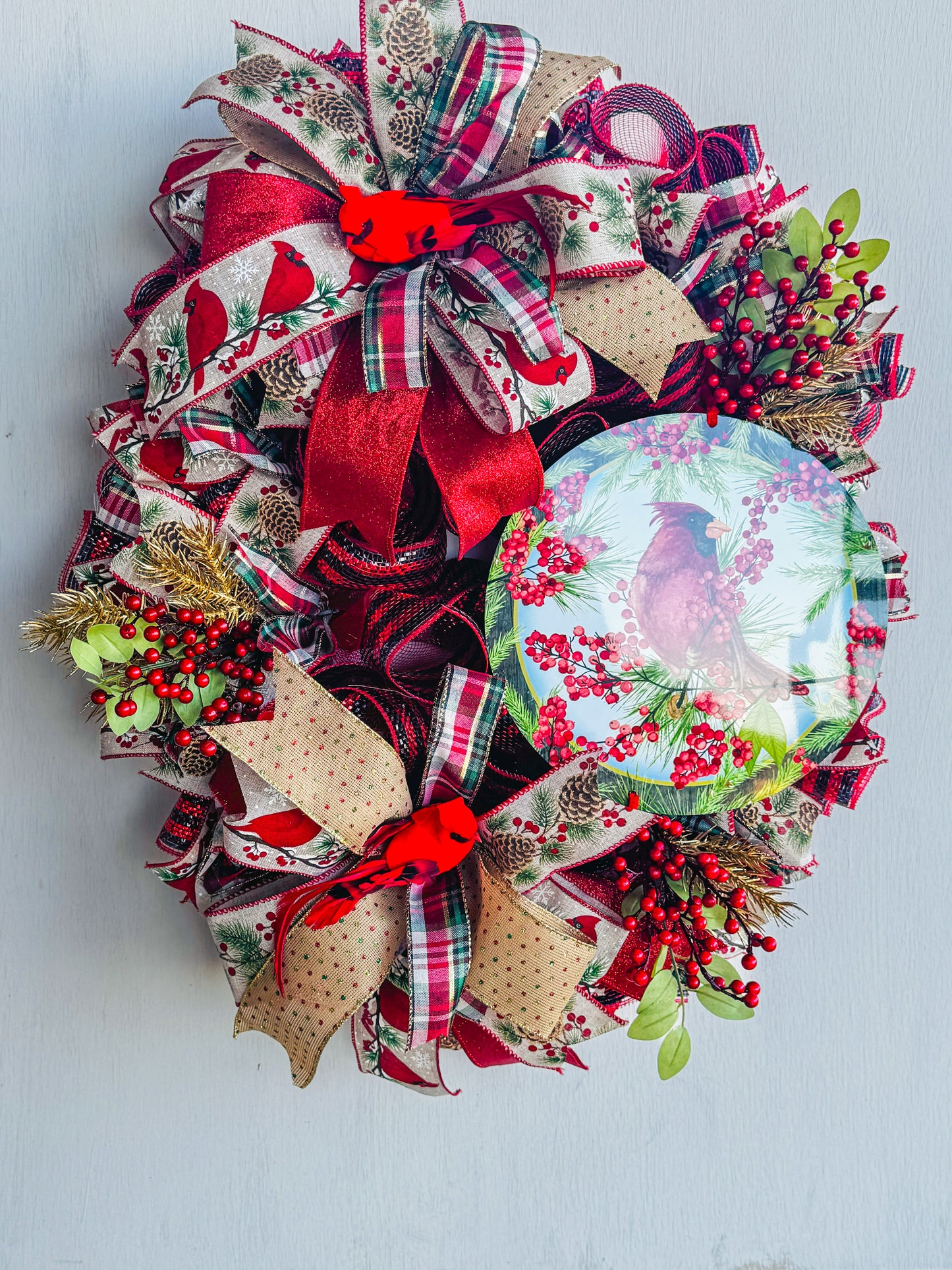 A symbol of hope and faith, this handcrafted cardinal wreath captures the beauty of Christmas with layered plaid ribbons, berry sprigs, and a vibrant cardinal centerpiece.