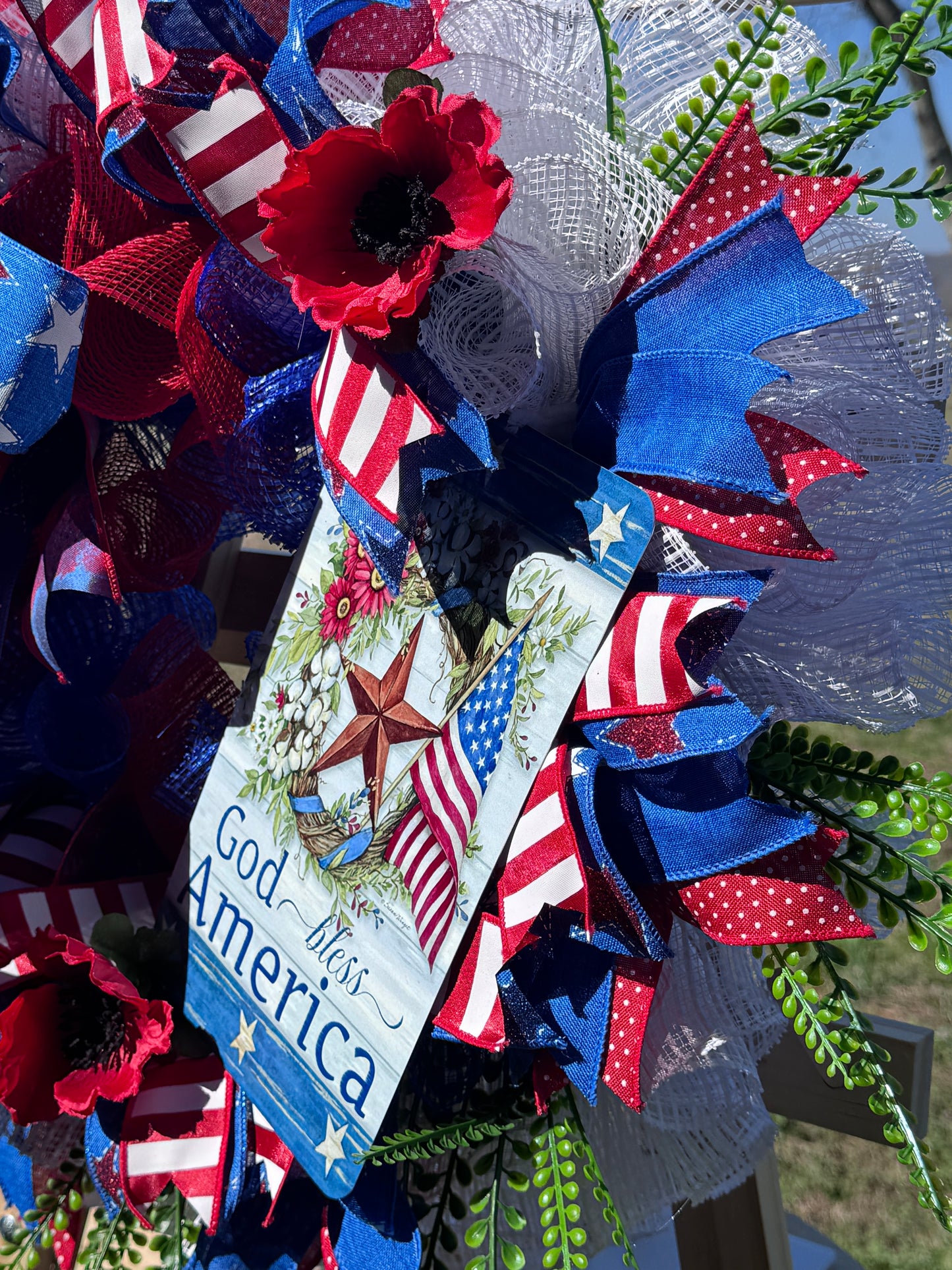 Patriotic wreath with red, white, and blue ribbons and a God Bless America sign.