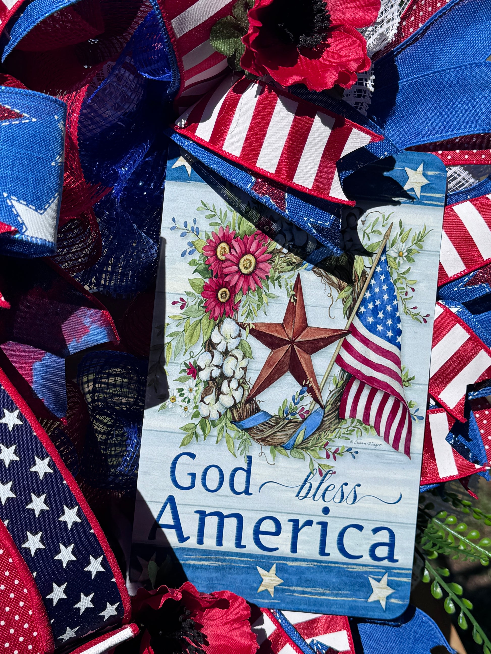 Patriotic tag reading God Bless America with flowers, stars, and American flag ribbons.