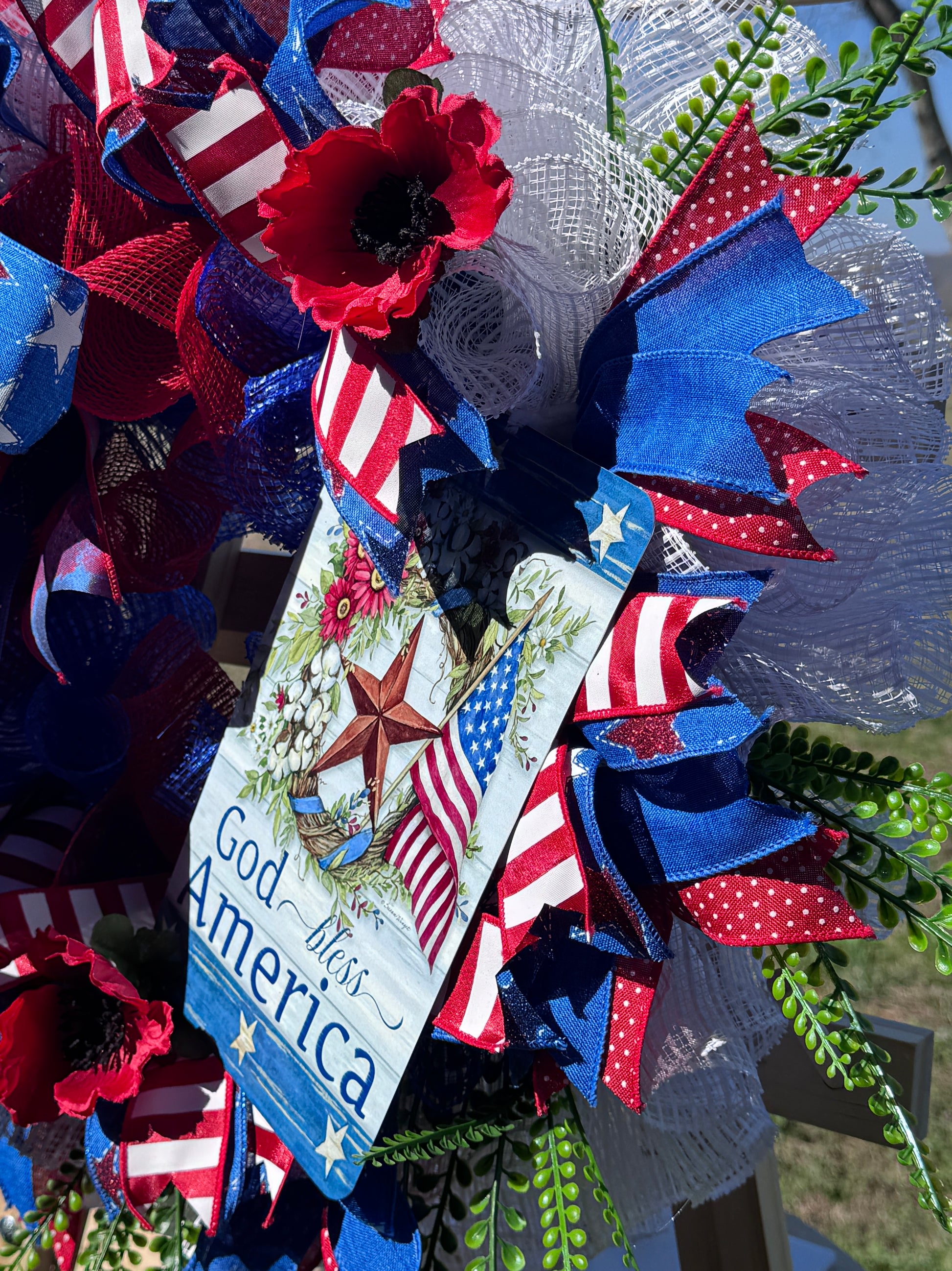 Patriotic wreath with red, white, and blue ribbons and a God Bless America sign.