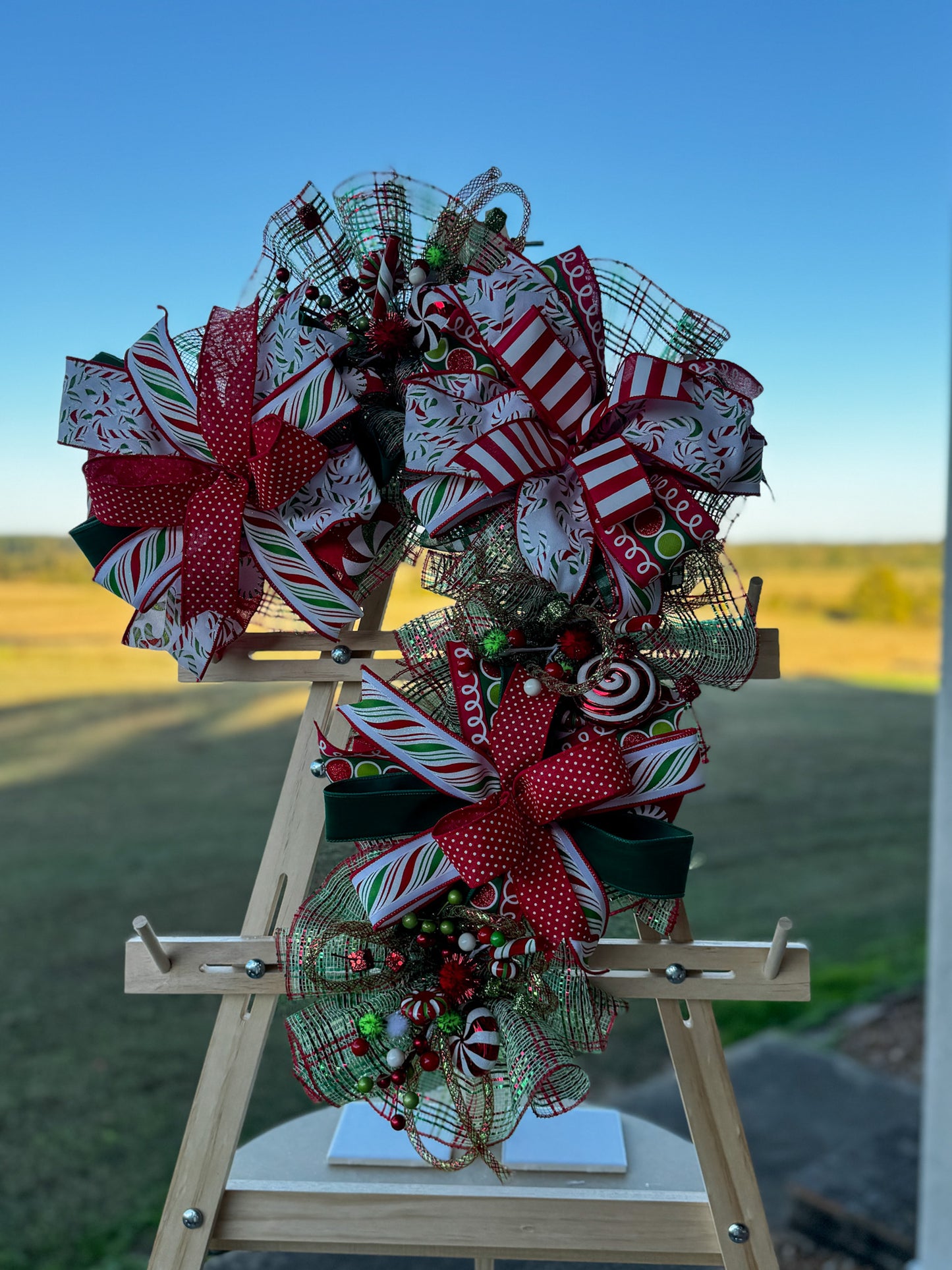 Whimsical handcrafted Candy Cane Swag with striped ribbon, glitter curls, and festive holiday accents. Playful, faith-inspired Christmas décor by Davis Wreath Creations.