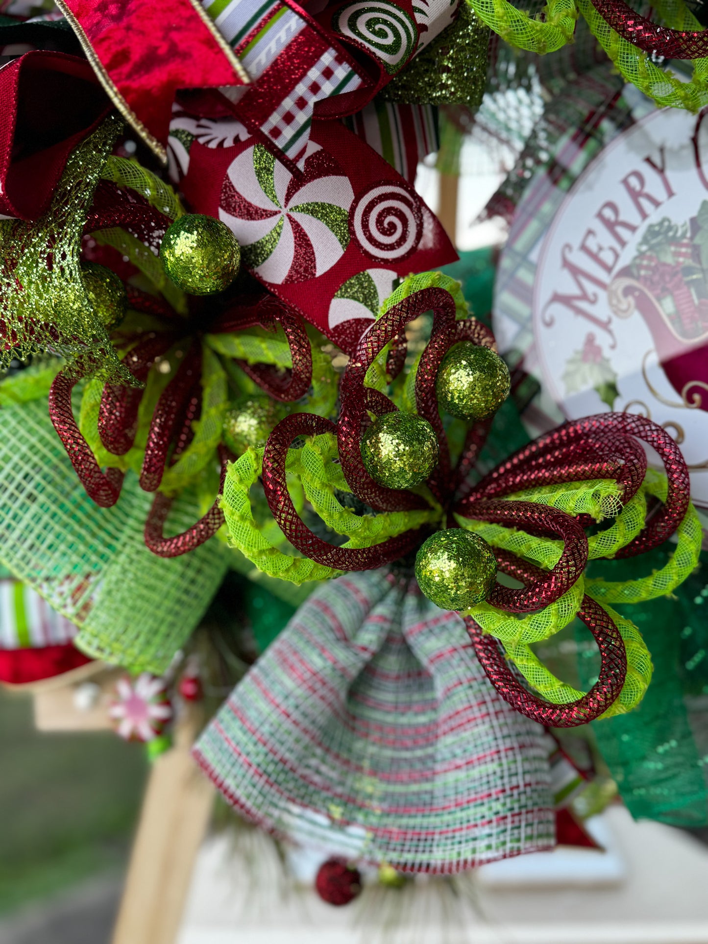 A burst of Christmas cheer! This Peppermint Twist Wreath blends playful red, green, and white ribbons with sparkling ornaments and a festive “Merry Christmas” sign — handcrafted to bring joy and color to your holiday door