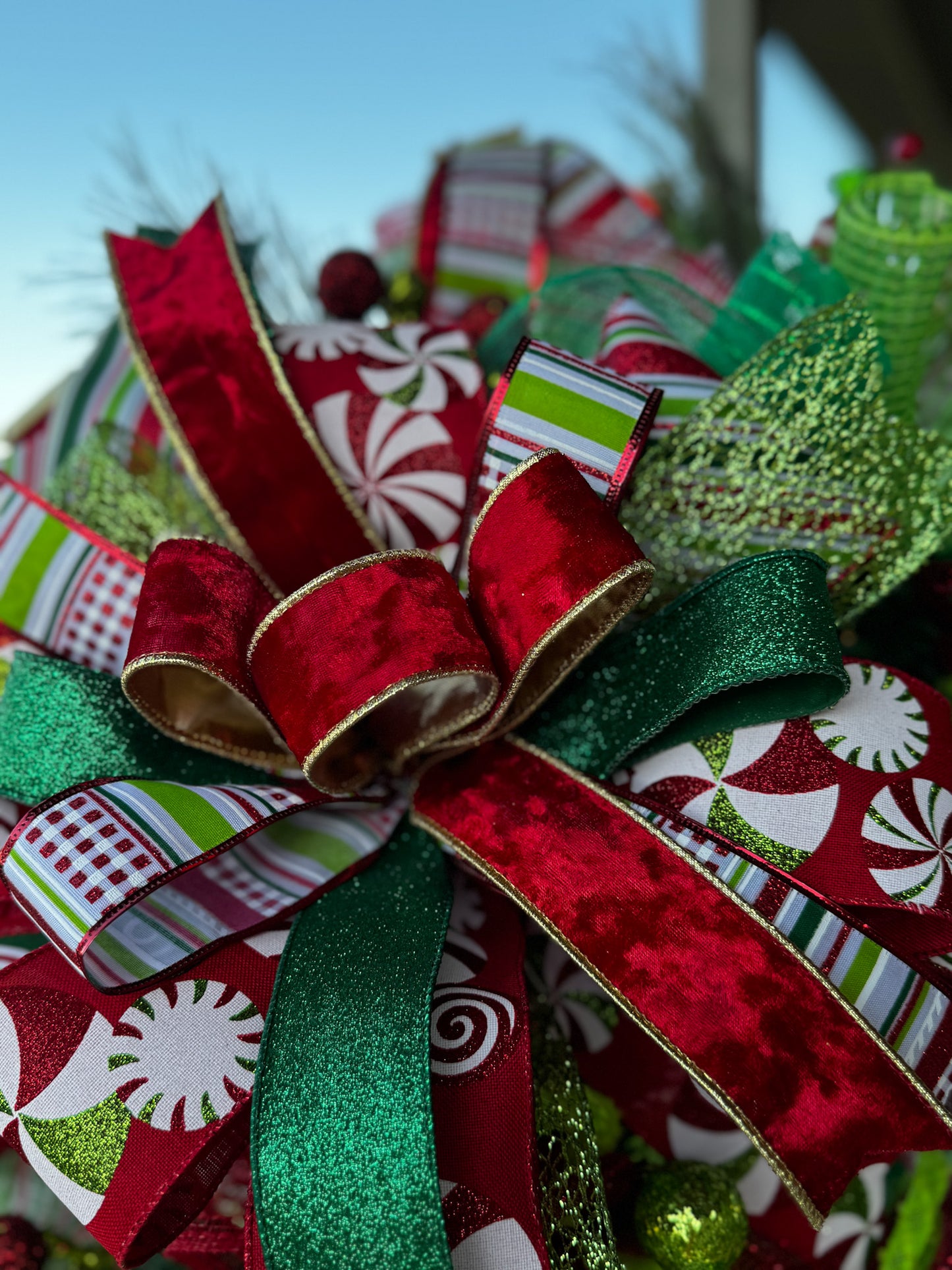 A burst of Christmas cheer! This Peppermint Twist Wreath blends playful red, green, and white ribbons with sparkling ornaments and a festive “Merry Christmas” sign — handcrafted to bring joy and color to your holiday door