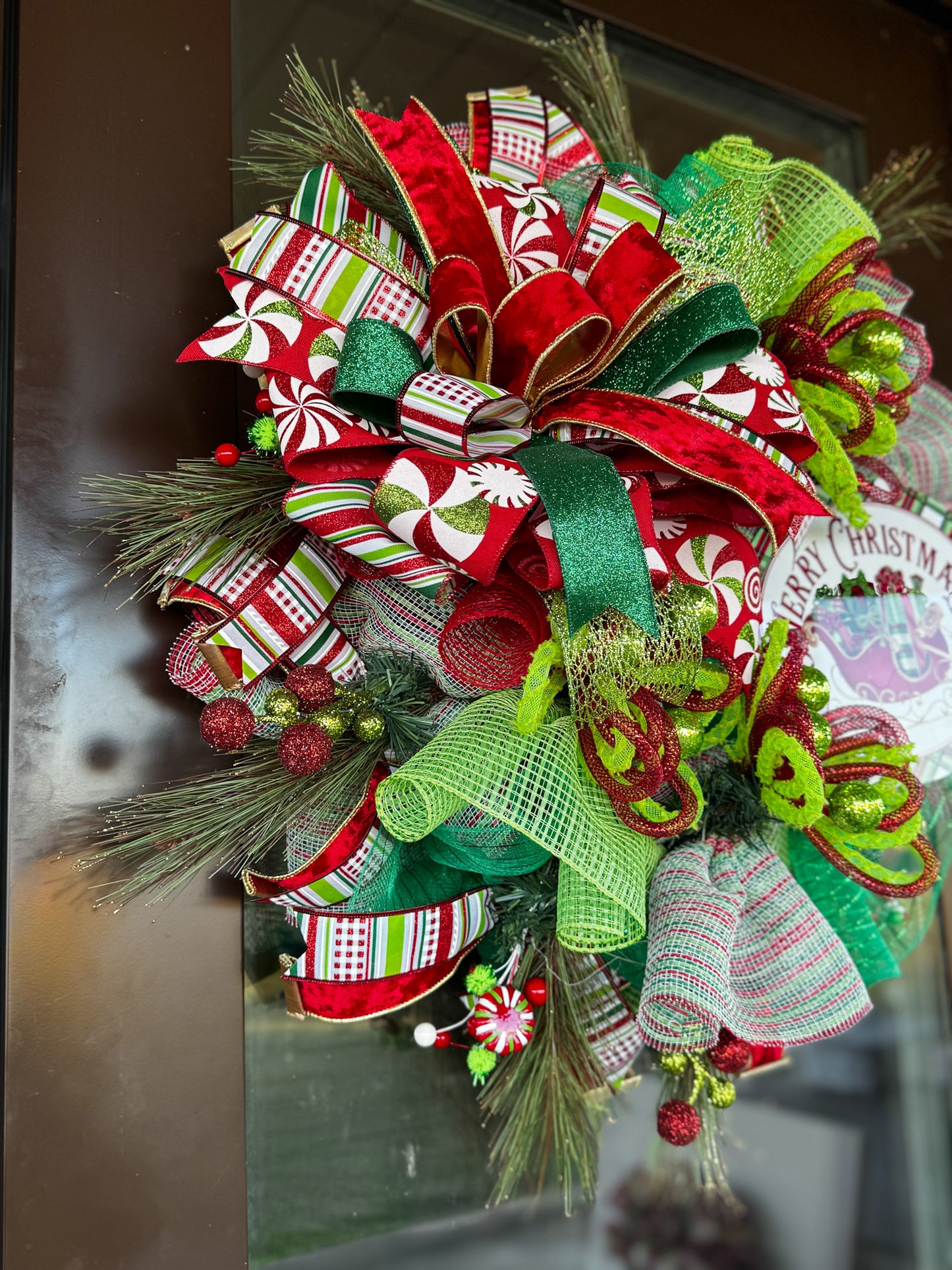 A burst of Christmas cheer! This Peppermint Twist Wreath blends playful red, green, and white ribbons with sparkling ornaments and a festive “Merry Christmas” sign — handcrafted to bring joy and color to your holiday door