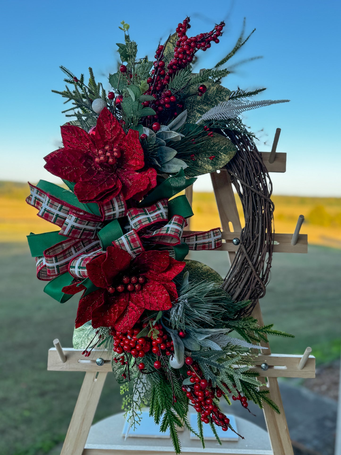 Two Poinsettia Christmas Grapevine Wreath:  Traditional Christmas beauty with a touch of handcrafted grace — this Two Poinsettia Grapevine Wreath features vibrant red poinsettias, lush greenery, and layered plaid ribbons in rich holiday tones.