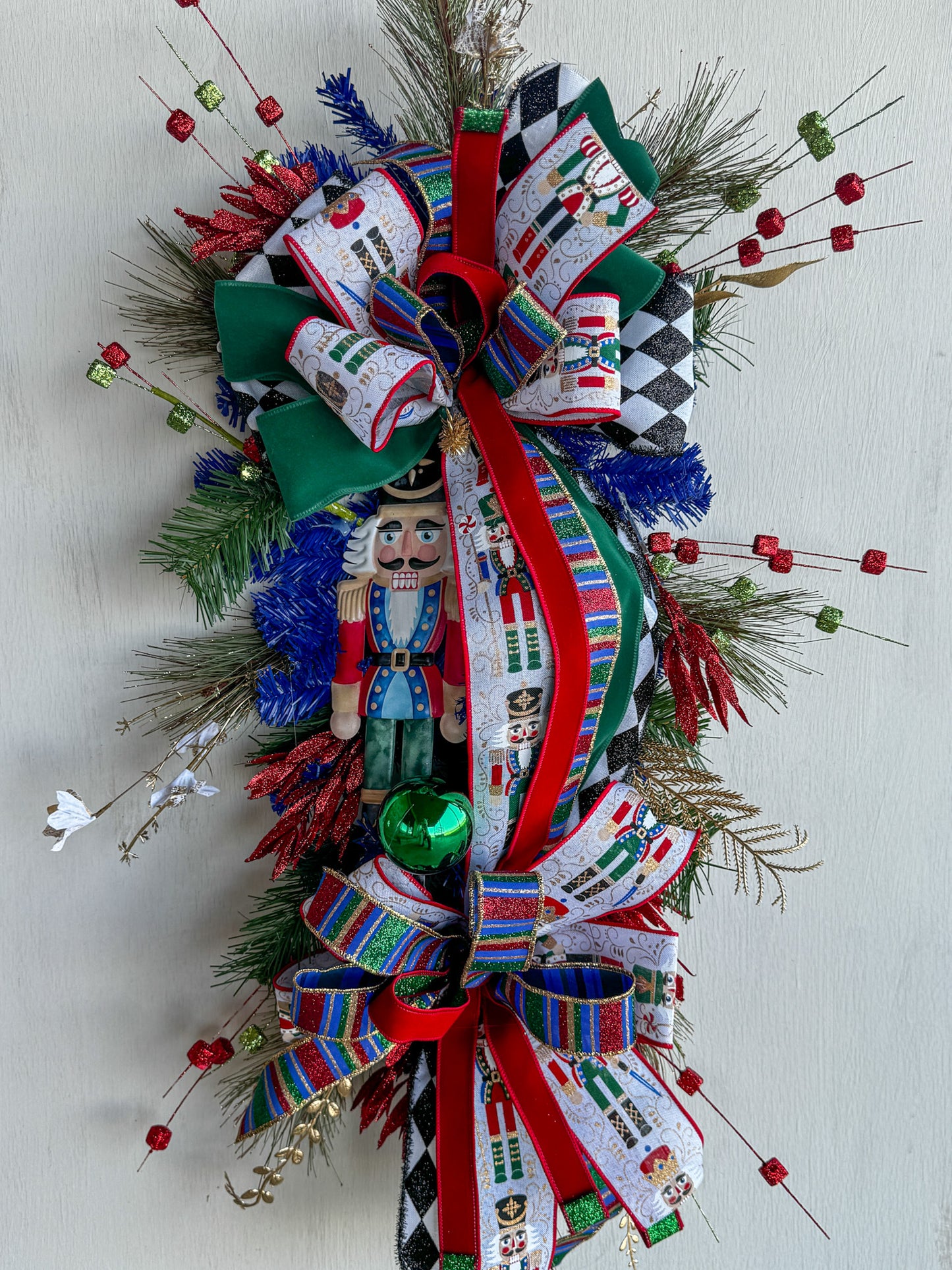 🎄 Nutcracker Teardrop Swag : A statement piece of Christmas elegance — this handcrafted Nutcracker swag blends classic charm with rich emerald velvet, harlequin ribbons, and glittering holiday details.