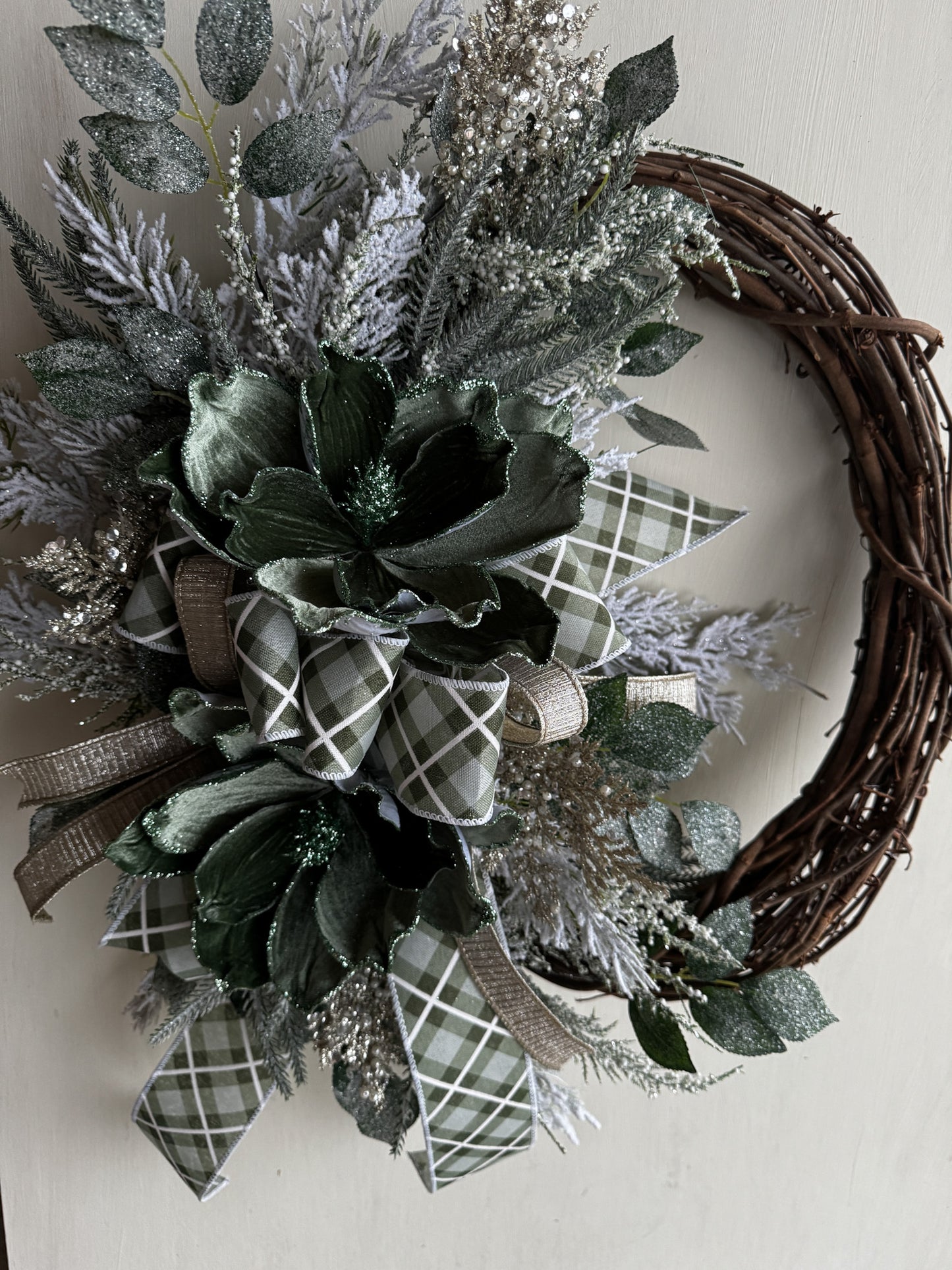 Winter Green Magnolia Grapevine Wreath with Jeweled Picks & Farrisilk Ribbon Short Description  Elegant, serene, and timeless — this handcrafted winter green magnolia wreath combines frosted greenery, jeweled accents, and luxurious Farrisilk ribbon.