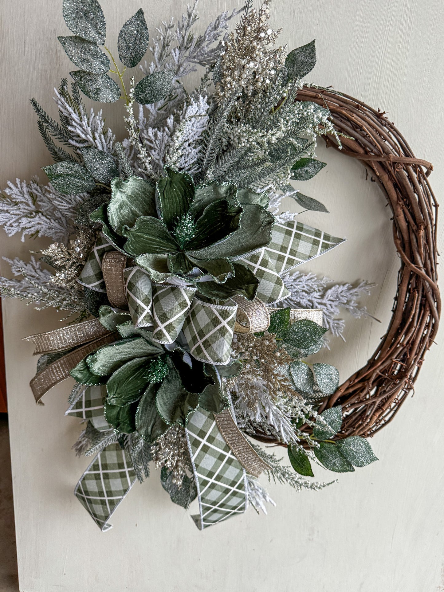 Winter Green Magnolia Grapevine Wreath with Jeweled Picks & Farrisilk Ribbon Short Description  Elegant, serene, and timeless — this handcrafted winter green magnolia wreath combines frosted greenery, jeweled accents, and luxurious Farrisilk ribbon.