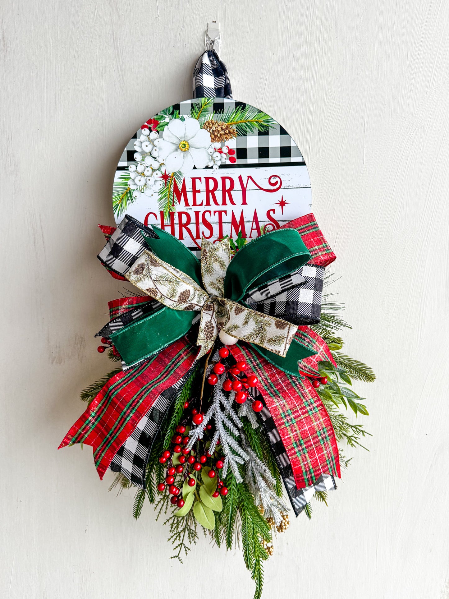 Celebrate the season with this charming Merry Christmas Sign — handcrafted with lush greenery, layered designer ribbons, and a festive metal sign. A perfect addition to farmhouse, traditional, or modern holiday décor.